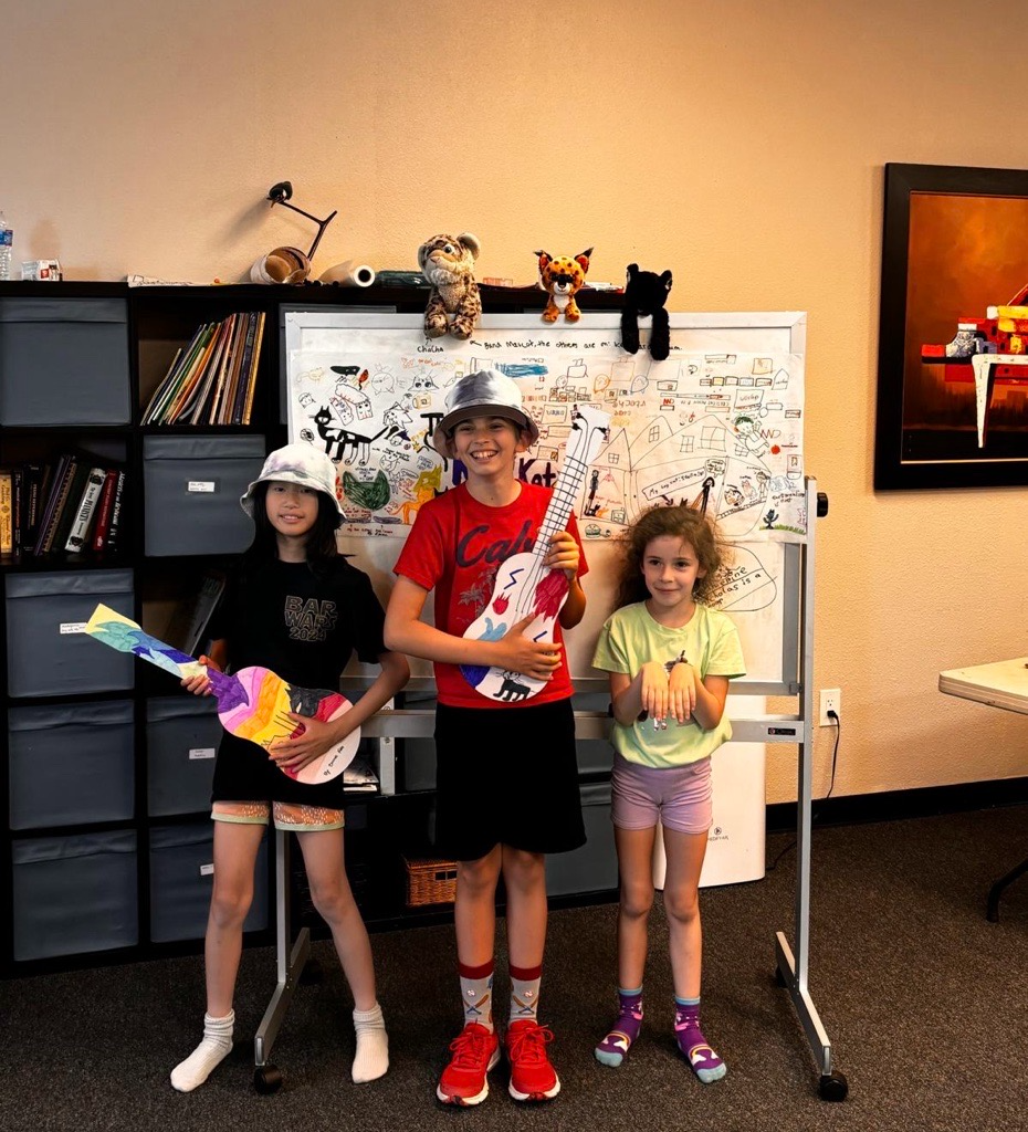Three young students holding handmade cardboard guitars in a music classroom