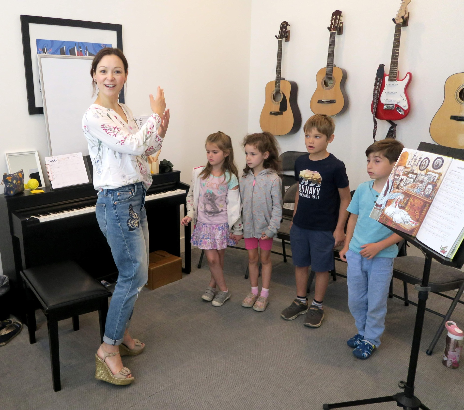 Music teacher leading a group of young children in a singing and movement activity in a bright music studio with guitars on the wall