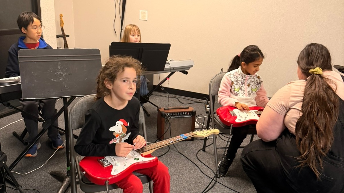 Instrument Exploration Program students learning guitar and keyboard with an instructor in a music classroom